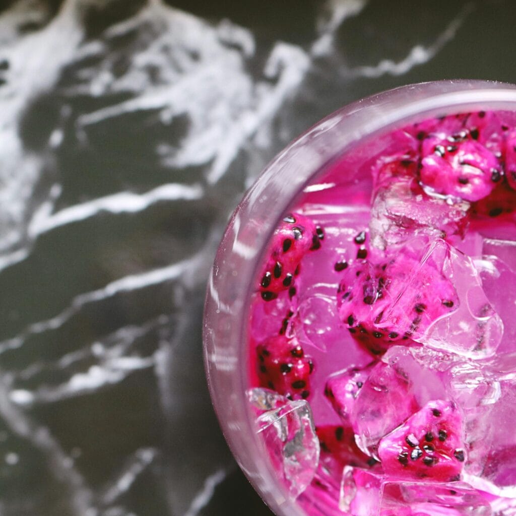 A vivid pink dragon fruit drink chilled with ice in a glass, offering a refreshing look.