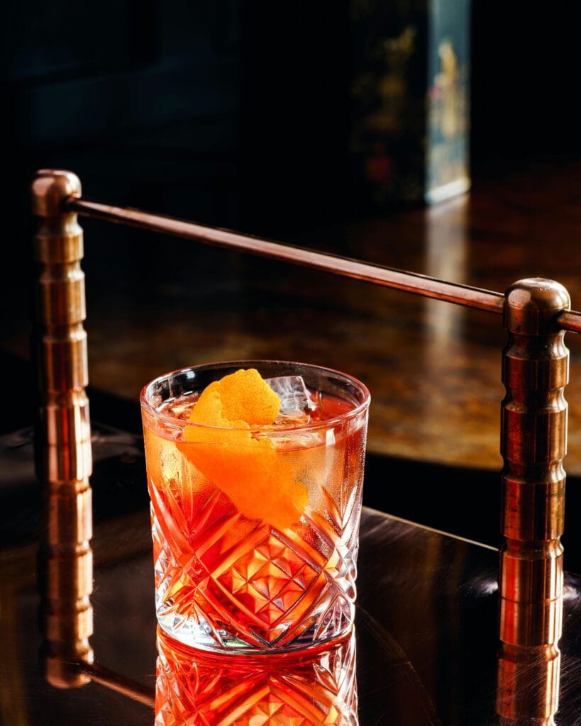 A sophisticated Negroni cocktail garnished with orange peel on a polished bar surface.