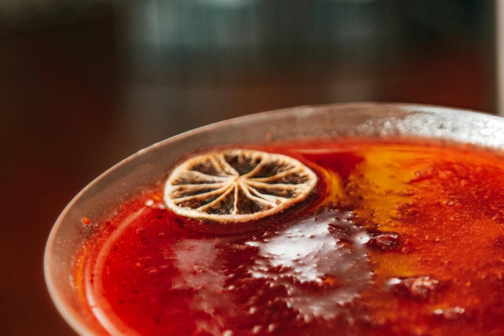 A vibrant red cocktail garnished with a dried citrus slice, highlighting texture and detail.
