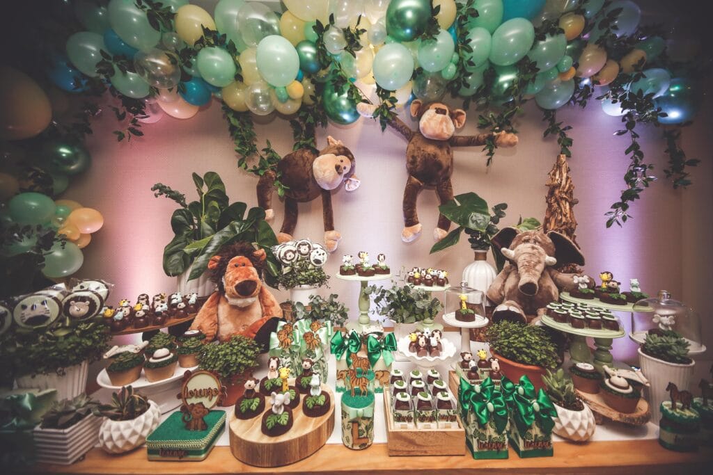 Whimsical jungle-themed dessert table for a birthday, featuring plush animals and green decorations.