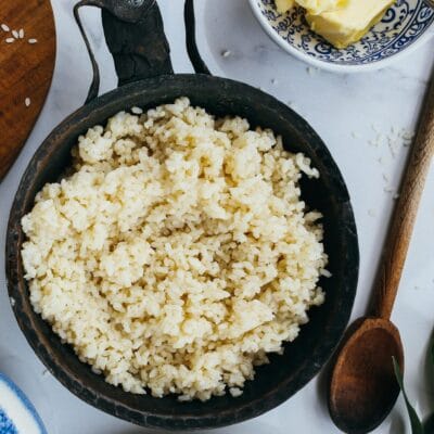 Flat lay of cooked rice in a frying pan with butter and tea on a wooden board.