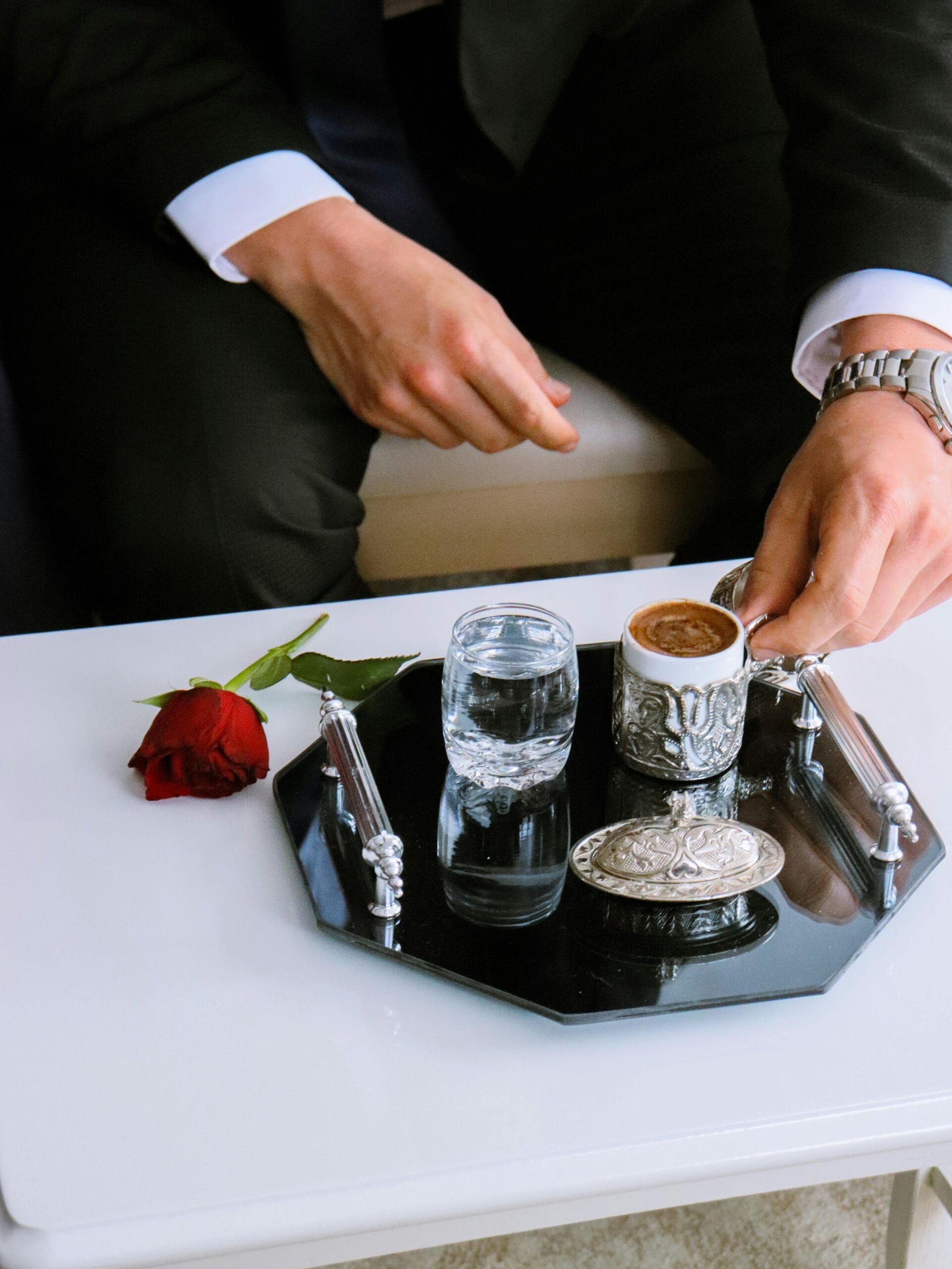 A refined coffee presentation on a silver tray with a red rose, ideal for luxury lifestyle themes.