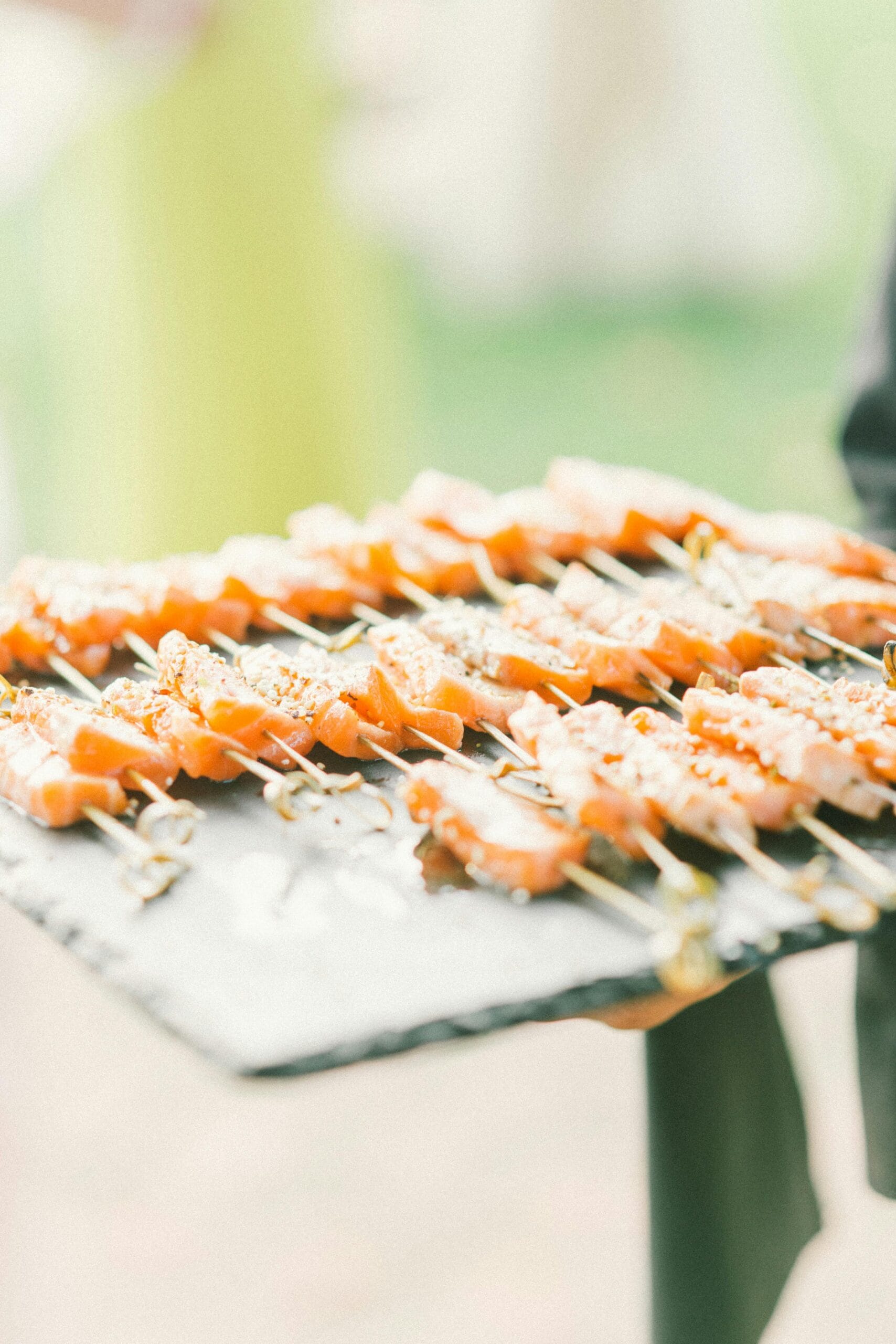 Close-up of gourmet salmon skewers served on a slate platter. Ideal for catering and events.